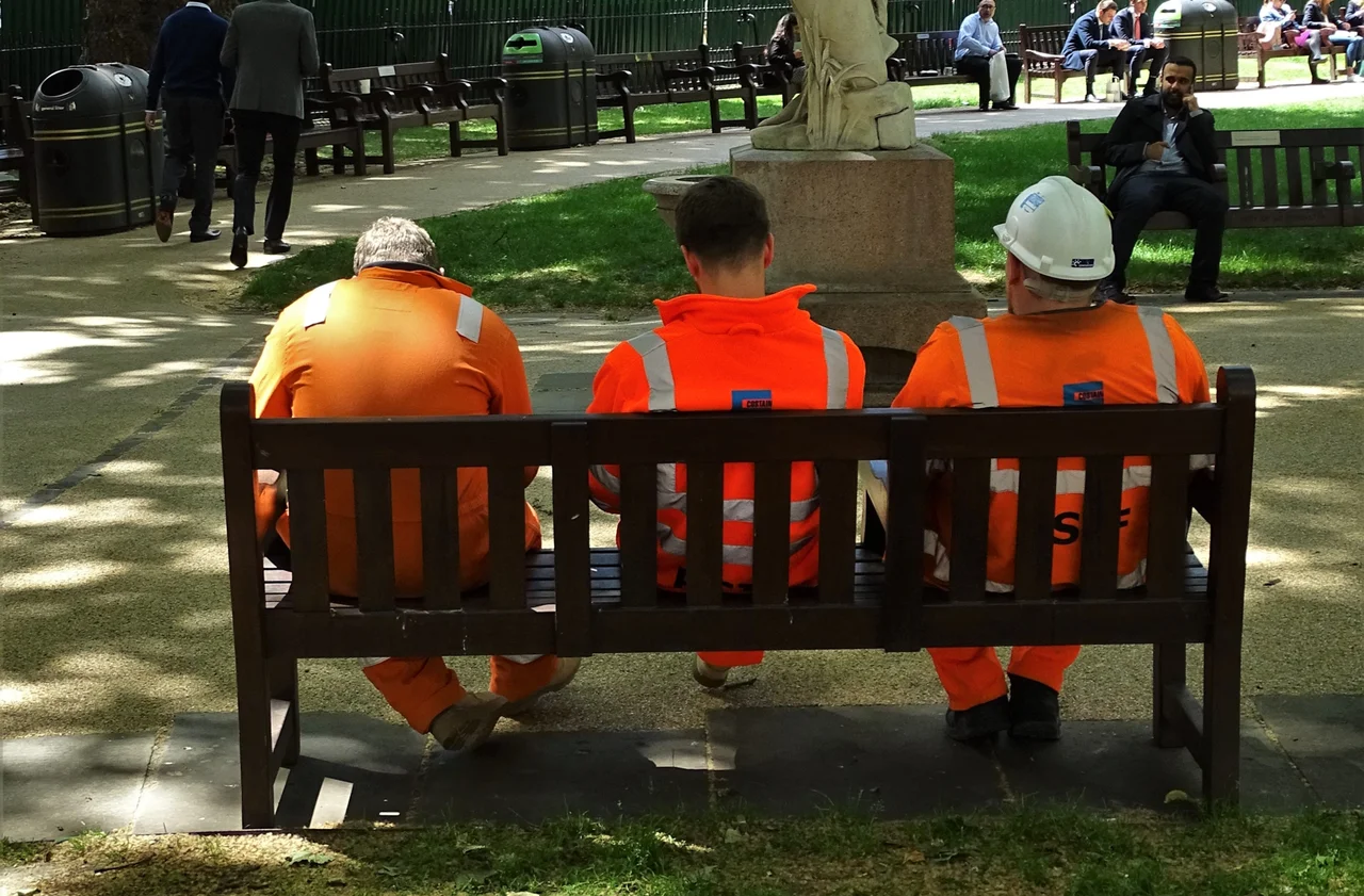 Three seated construction workers seen from behind in high-visibility clothing in London, June 2019