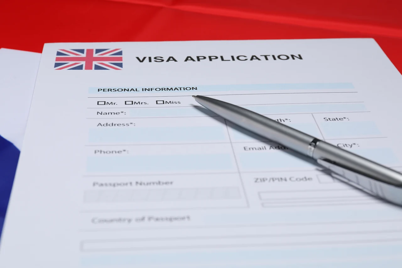 Staged blank generic visa application sheet with a Union Jack and silver pen on red, white and blue fabric. No worker, applicant or actual government record is pictured.